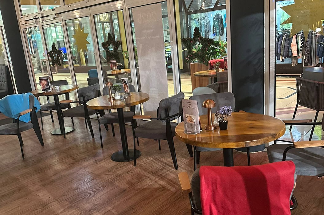 Ein gemütliches Café, leere Sitzplätze, Holztische, rote Decke, Fenster mit weihnachtlicher Deko.
